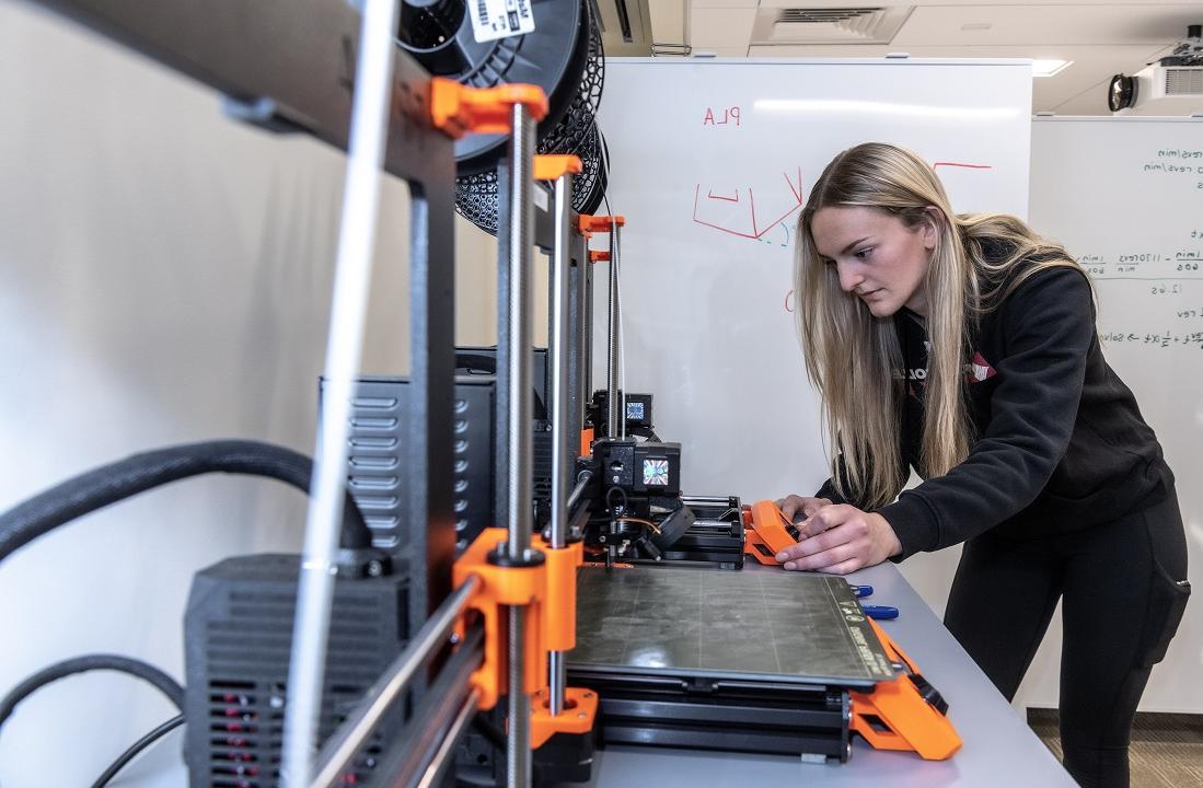 Photoshoot of Ashley Waldron '26 (MCAS) in the Service Building annex of 245 Beacon St. showing the 3D printer that was the equipment that was used to form Ashley's hockey invention.